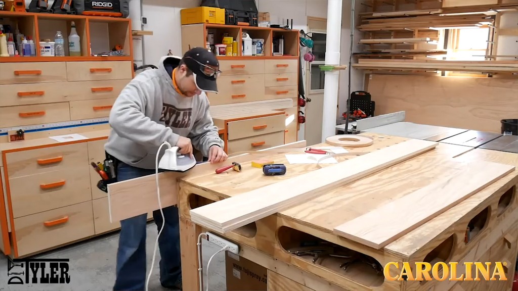 man running clothing iron along edge of plywood board